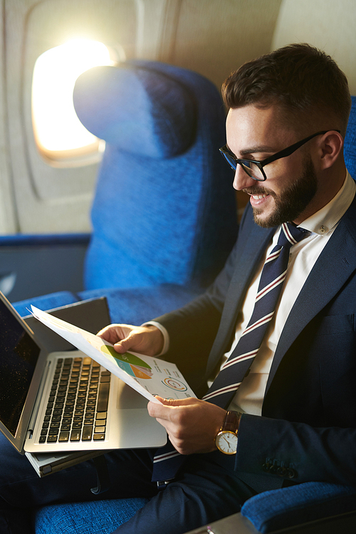 High angle portrait  of smiling bearded businessman working while enjoying flight in first class, copy space