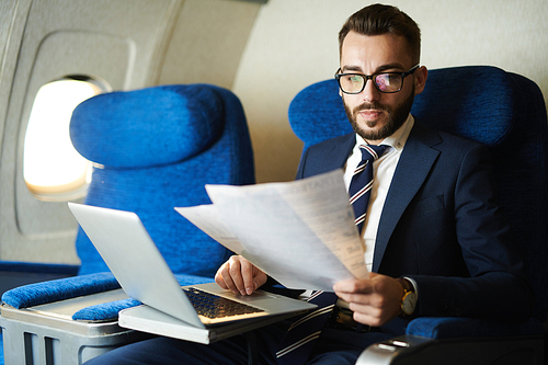 Portrait  of handsome bearded businessman reading document and working while enjoying flight in first class, copy space