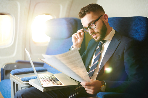 Side view portrait  of handsome bearded businessman reading document and working while enjoying flight in first class, copy space