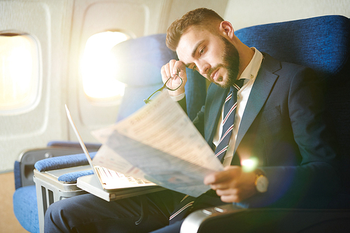 Side view portrait  tired handsome businessman reading document and working while sitting in first class during flight, copy space