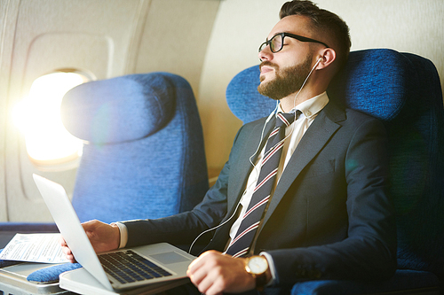 Portrait of handsome bearded businessman listening to music and relaxing  in first class flight, copy space