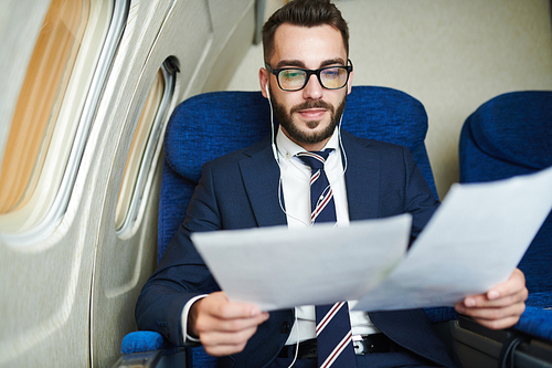 Portrait of handsome bearded businessman reading documents while working in plane, copy space