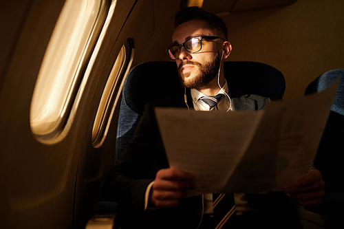 Portrait of modern successful  businessman looking in window while flying by first class plane at night, copy space