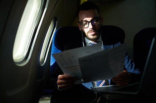 Portrait of successful young businessman working in dark plane while enjoying first class flight, copy space