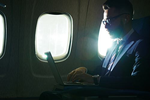 Side view portrait of successful young businessman working during flight in dimly lit plane, copy space