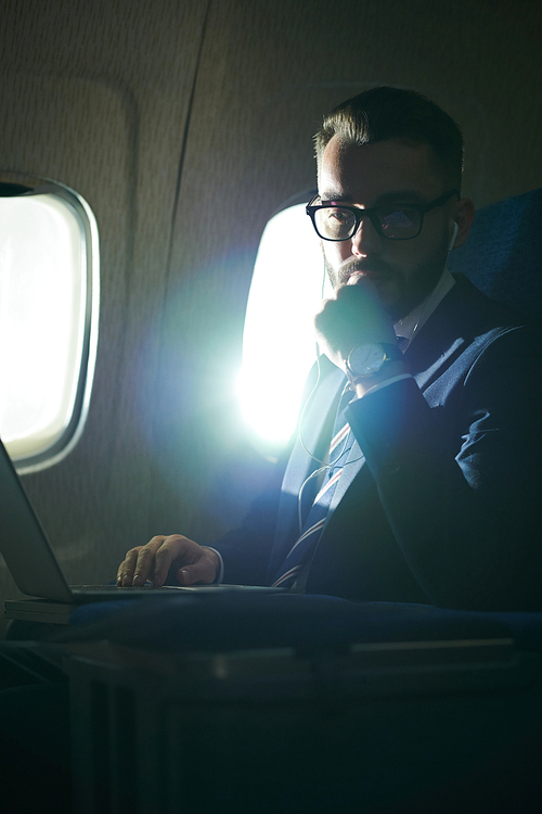 Portrait of pensive businessman sitting in first class during flight in dimly lit plane, copy space