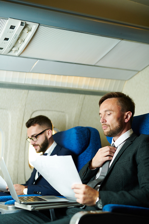 Portrait of two modern business people working in plane during first class flight, focus on handsome man in front, copy space