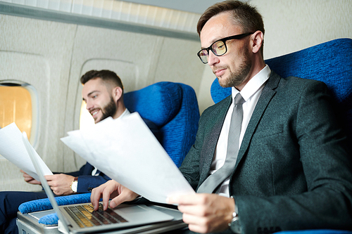 Portrait of two business people working and reading  documents  in plane during first class flight, copy space