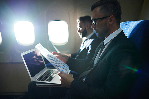 Side view portrait of two business people working and reading  documents  in dimly lit plane during first class flight, copy space