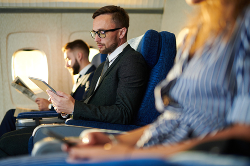 Row of people sitting in plane, focus of handsome businessman using digital tablet, copy space