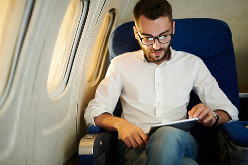 Portrait of handsome bearded man using digital tablet while enjoying first class flight by sunset, copy space