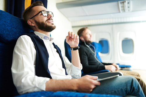 Side view portrait of handsome bearded man smiling happily while enjoying first class flight sitting in comfortable seat of modern plane, copy space