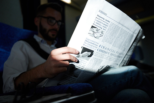Close up of unrecognizable man holding business newspaper  while reading in plane, shot with flash, copy space