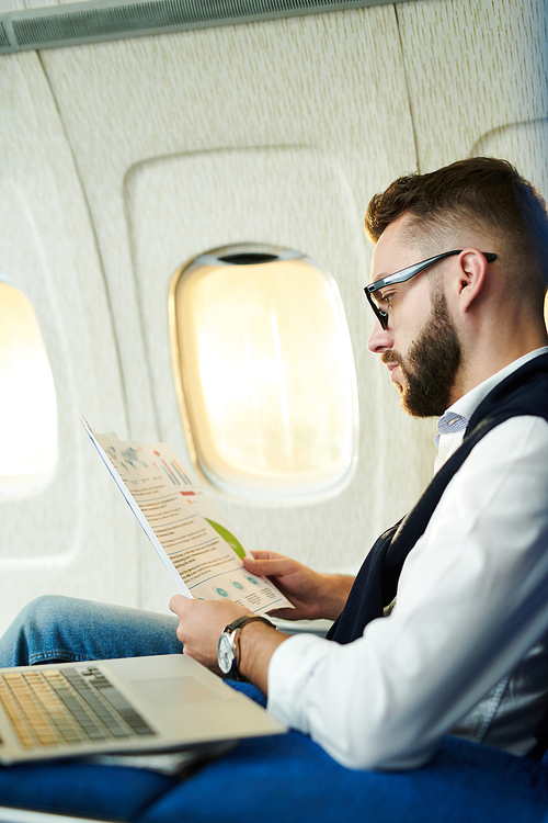 Side view portrait  handsome businessman reading marketing reports while working in plane during long flight, copy space