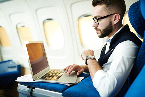 Side view portrait  of handsome businessman using laptop while working in plane during long first class flight, copy space