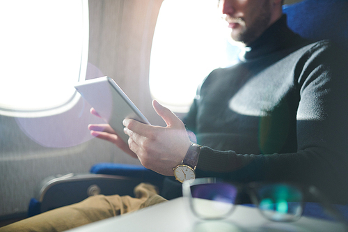 Mid section portrait of unrecognizable man using digital tablet while enjoying long first clas flight in plane, copy space
