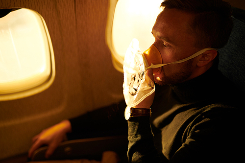 Side view portrait of mature man wearing oxygen mask in plane, copy space