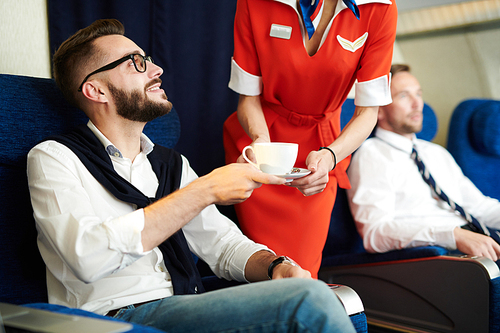 Portrait of handsome businessman smiling while taking coffee served by flight attendant in first class, copy space
