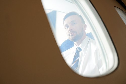 Portrait of handsome man looking at window in plane during take-off or landing, view from outside, copy space