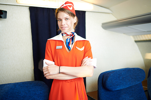 Waist up portrait of young female flight attendant posing on board of plane smiling at camera, copy space
