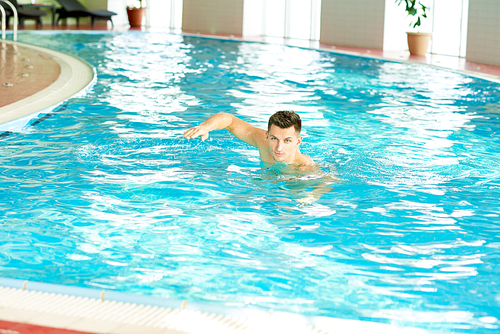 Portrait of handsome young man swimming in indoor pool at health club, , copy space
