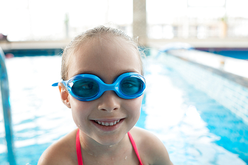 Cheerful active pretty girl in swimming goggles smiling at camera in modern indoor pool with clean water