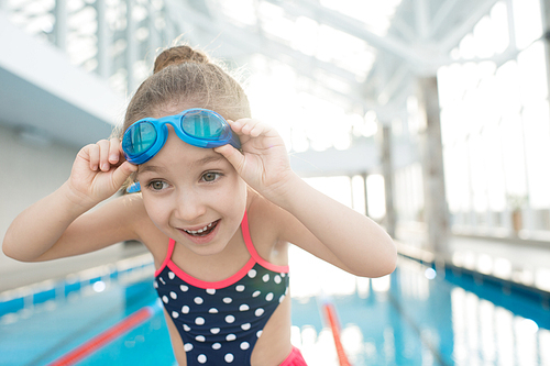 Cheerful emotional girl adjusting swimming goggles and preparing for training on pool enjoying this activity
