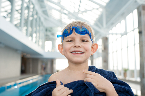 Head and shoulders portrait of smiling little boy wearing goggles  while drying with towel after completion of swimming training
