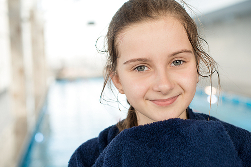 Portrait of content beautiful kid with wet hair wrapped in bath towel and standing in swimming pool