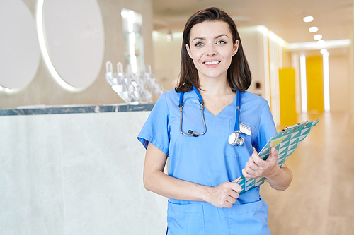 Waist up portrait of  young female medic  and smiling cheerfully while posing in hall of modern clinic