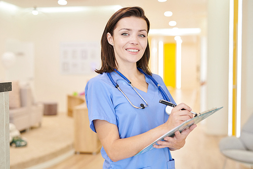 Waist up portrait of smiling female medic  while posing in hall of modern clinic, copy space