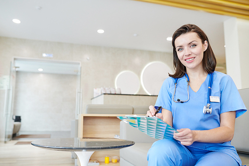 Portrait of smiling female medic  while sitting in hall of modern clinic, copy space