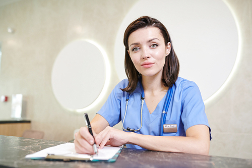 Portrait of female medic  and smiling while working at desk in modern clinic, copy space