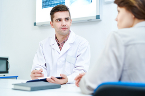 Portrait of young doctor listening to patients symptoms sitting at desk in office, copy space