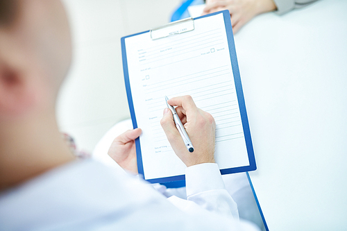 Close up of unrecognizable doctor writing on clipboard while consulting patient in office