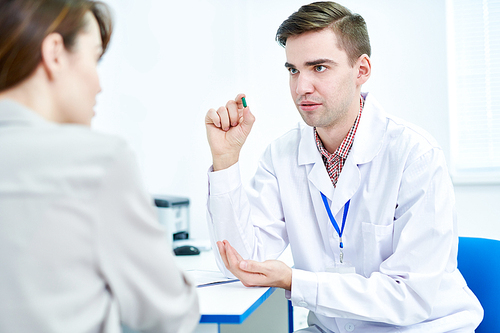 Portrait of doctor offering pills and medication  to young woman while sitting at desk in office, copy space