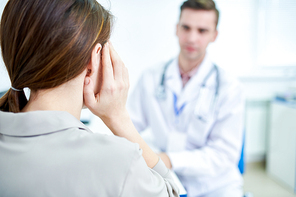Back view portrait of young woman suffering from headache talking to doctor in clinic, copy space