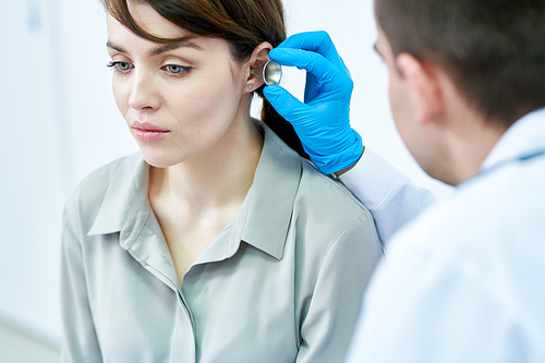 Portrait of beautiful young woman having her ears and hearing tested by doctor in clinic, copy space