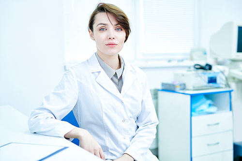 Female medic in white coat sitting at desk in office and .