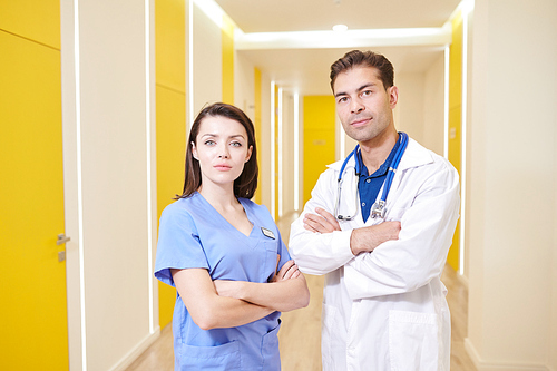 Waist up portrait of female nurse and doctor posing  while standing with arms crossed in hall of modern clinic, copy space