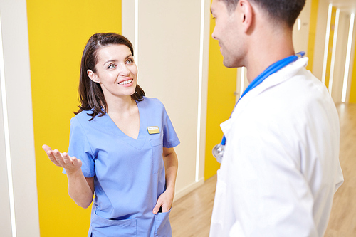 Portrait of smiling young nurse talking to doctor in hall of modern clinic, copy space