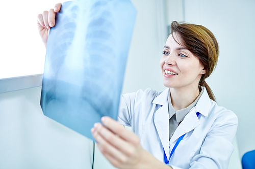 Female medic holding X-ray image of chest looking at it and smiling.