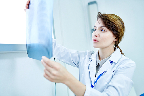 Female medic holding X-ray image of chest and examining it carefully.