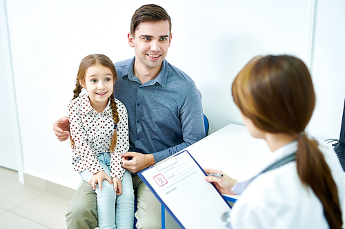 Little girl sitting on father lap and listening attentively to doctor