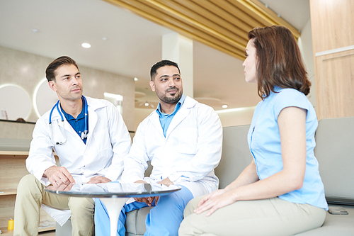 Portrait of two doctors listening to female patient during medical examination in modern clinic, copy space