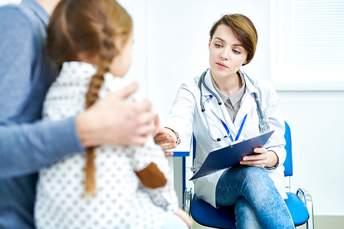 Crop view of female doctor sitting in office and listening to small patient