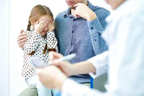 Crop close-up view of young dad hugging scared daughter with close eyes by hands