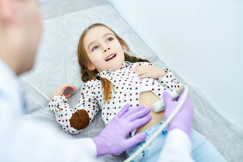 Crop close-up view of doctor examining little girl lying on medical couch