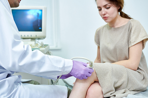 Crop blur view of medical specialist checking knee of beautiful female by device