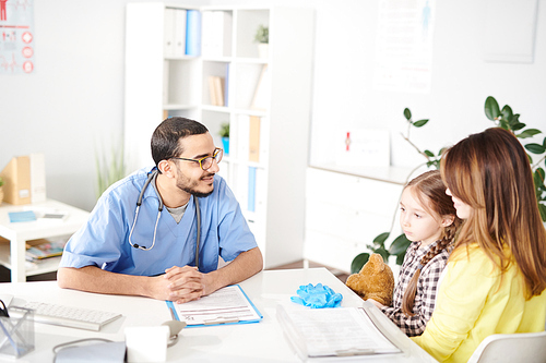 Portrait of smiling Middle-Eastern pediatrician talking to young mother and little girl during consultation in modern clinic, copy space